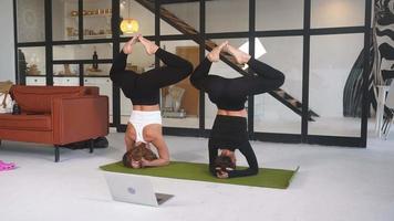 Two young women work out on a yoga mat on the floor with an open laptop nearby video