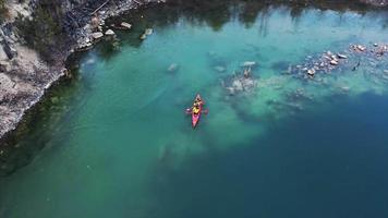 People in orange kayak paddle in flooded rock quarry video