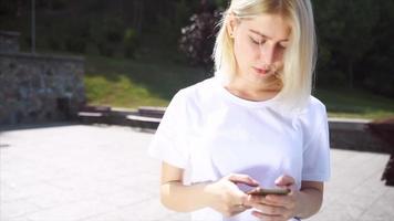 joven rubia o adolescente mira hacia arriba a los mensajes de texto del teléfono bajo el sol brillante video