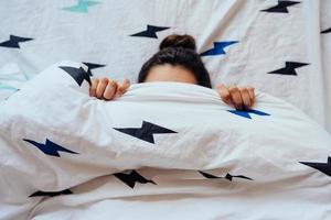 el primer plano de una encantadora joven yace en la cama cubierta con una manta. foto