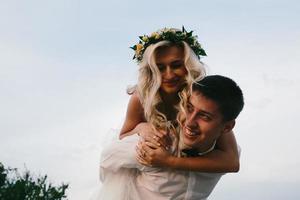 groom carries bride on his back outdoors photo