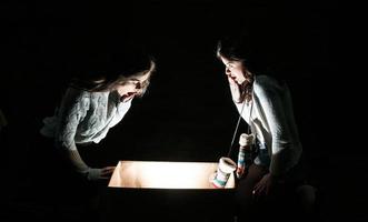 Sisters opens a box with a Christmas present and fascinated looks inside photo