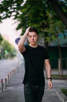 Young adult man in a black t-shirt and jeans walks on a city street photo