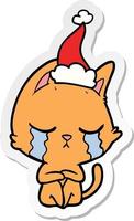 crying sticker cartoon of a cat sitting wearing santa hat vector