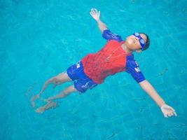 niño con traje de baño y gafas nadando en medio de la piscina con un fondo de agua azul foto