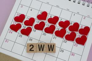Palabra 2ww en bloque de madera con forma de corazón rojo en el calendario. concepto de espera de dos semanas foto