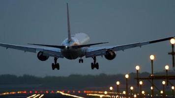 The wide bodied aircraft lands on the illuminated runway in the early morning video