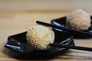 Close up of fresh deep fried sesame balls or jian dui lying on dark plates against a light background with chopsticks photo