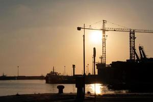 January 4th, 2021, in Mazara del Vallo, Sicily, the sun sets behind the port in the evening and shines a red light on the ships in front of the sea photo