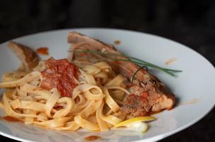 A lunch with lamb ribs on ribbon noodles with tomato sauce in front of a dark background photo