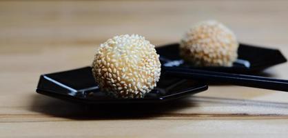 Close up of fresh deep fried sesame balls or jian dui lying on dark plates against a light background with chopsticks photo