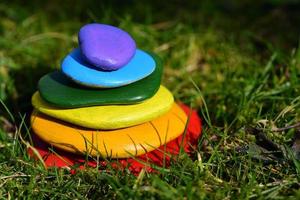 Several brightly colored pebbles painted in rainbow colors lie on top of one another in a meadow with green grass photo