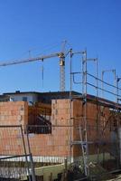 Close up of the shell of a stone house on a construction site for a residential area, with a blue sky and crane in the background photo