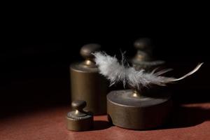 Several metal weights stand in front of a dark background with space for text and above it lies a white bird's feather photo