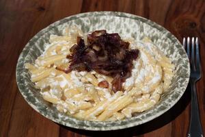 A plate of pasta and ricotta, as well as roasted onions, is on a wooden table, with a fork next to it, ready to eat photo