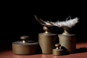 Several metal weights stand in front of a dark background with space for text and above it lies a white bird's feather photo