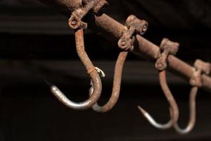 Rusty meat hooks hang from the ceiling against a dark background photo