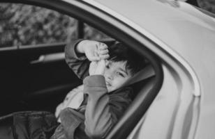 Black and White Portrait Happy boy siting in safety car seat looking at camera with smiling face,Child sitting in the back passenger seat with a safety belt, School kid traveling to school by car photo