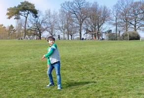 niño feliz jugando en el parque, niño divirtiéndose jugando afuera en la primavera soleada, niño de la escuela diviértase con un disco volador en el campo en verano, deporte y recreación al aire libre actividad para el concepto de niños foto