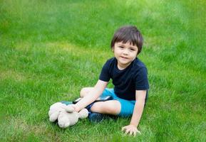 Kid sitting on grass using tablet for his homework in the garden on spring, Child boy playing  teddy bear toy in the park in sunny day summer, Home schooling,Social Distance photo