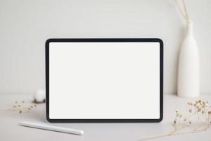 tableta pantalla blanca vacía con maqueta de lápiz. flor de algodón y hojas secas en la maqueta de fondo beige para el diseño foto