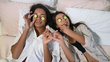 Home spa. Two women holding pieces of cucumber on their faces lying the bed. photo