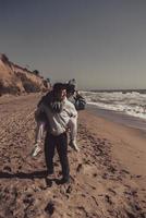 Man carries his girlfriend on back, couple having fun on the seashore photo