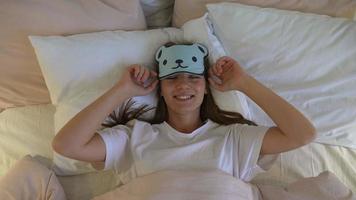 Happy sleepy young adult woman waking up lying in white bed photo