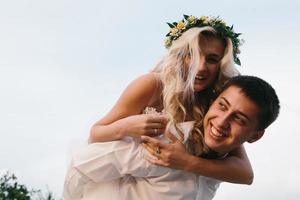 el novio lleva a la novia en la espalda al aire libre foto