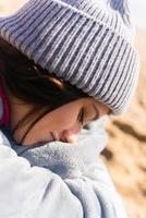 Pretty woman in warm clothes sitting on the cold beach. photo