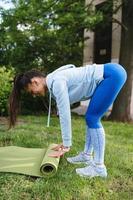 Woman folding roll fitness or yoga mat after working out in the park. photo