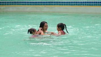 familia asiática divirtiéndose en la piscina. madre enseñando a sus hijas a nadar. familia feliz pasó las vacaciones de verano juntos. video