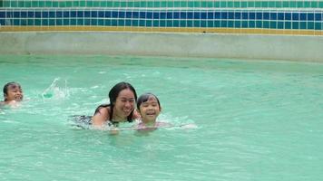 familia asiática divirtiéndose en la piscina. madre enseñando a sus hijas a nadar. familia feliz pasó las vacaciones de verano juntos. video