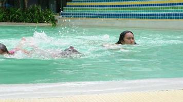 asiatico famiglia avendo divertimento nel nuoto piscina. madre insegnamento sua figlie Come per nuotare. contento famiglia speso il estate vacanza insieme. video