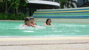 asiatische familie, die spaß im schwimmbad hat. Mutter bringt ihren Töchtern das Schwimmen bei. Glückliche Familie verbrachte die Sommerferien zusammen. video