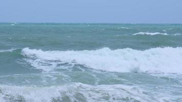 vagues de l'océan et sable sur la plage des mers tropicales en thaïlande. de fortes vagues de la mer s'écrasent sur le rivage pendant la saison des pluies. video