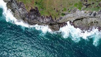 vista aérea de las olas del mar rompiendo en el acantilado de rocas en el océano azul. vista superior de las rocas costeras en el océano de phuket. punto de vista del paisaje del cabo laem phromthep en la mañana. video