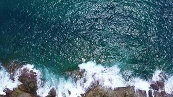 luftaufnahme von meereswellen, die auf einer felsenklippe im blauen ozean zusammenstoßen. Blick von oben auf die Küstenfelsen im Ozean von Phuket. landschaftsaussichtspunkt von laem phromthep cap am morgen. video