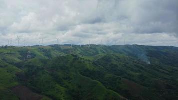 vista aérea de la granja de molinos de viento para la producción de energía en la montaña con cielo nublado. campos de aerogeneradores khao kho en tailandia. Las turbinas eólicas producen energía renovable limpia para el desarrollo sostenible. video