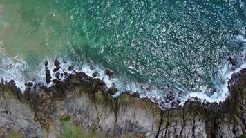 vista aérea das ondas do mar batendo no penhasco de rochas no oceano azul. vista superior das rochas costeiras no oceano de phuket. ponto de vista da paisagem de laem phromthep cape pela manhã. video