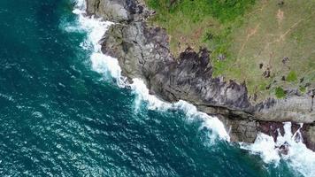 vista aérea de las olas del mar rompiendo en el acantilado de rocas en el océano azul. vista superior de las rocas costeras en el océano de phuket. punto de vista del paisaje del cabo laem phromthep por la mañana. video