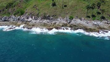 luftaufnahme von meereswellen, die auf einer felsenklippe im blauen ozean zusammenstoßen. Blick von oben auf die Küstenfelsen im Ozean von Phuket. landschaftsaussichtspunkt von laem phromthep cap am morgen. video