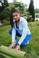 Woman folding roll fitness or yoga mat after working out in the park. photo