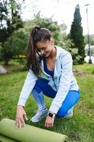 Woman folding roll fitness or yoga mat after working out in the park. photo