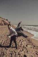 el hombre lleva a su novia en la espalda, pareja divirtiéndose en la orilla del mar foto