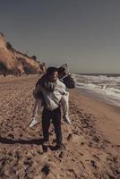 Man carries his girlfriend on back, couple having fun on the seashore photo