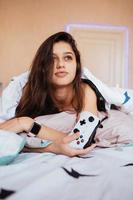 Funny girl lying in bed and playing video game, holding controller photo