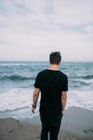 Smiling guy in a black T-shirt stands on the sandy seashore. photo