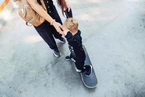 Young mother teaches her little boy to ride a skateboard photo