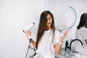 Young beautiful woman in the bathroom holding a hairdryer and a small bottle photo